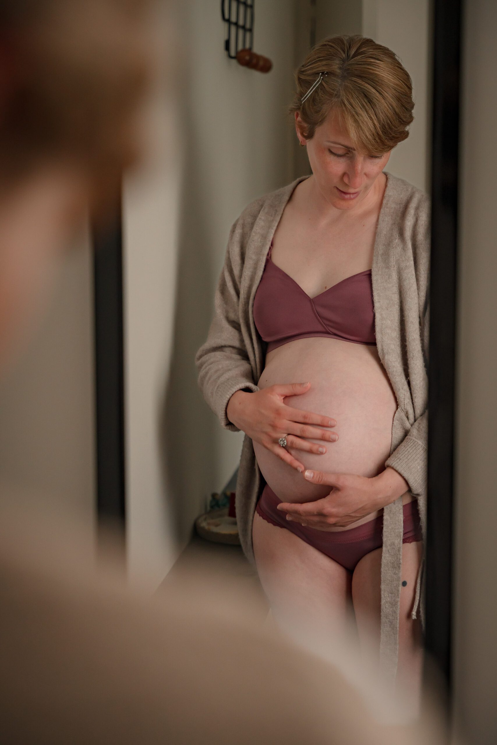 Séance photo grossesse d'une femme enceinte qui tient son ventre face au miroir