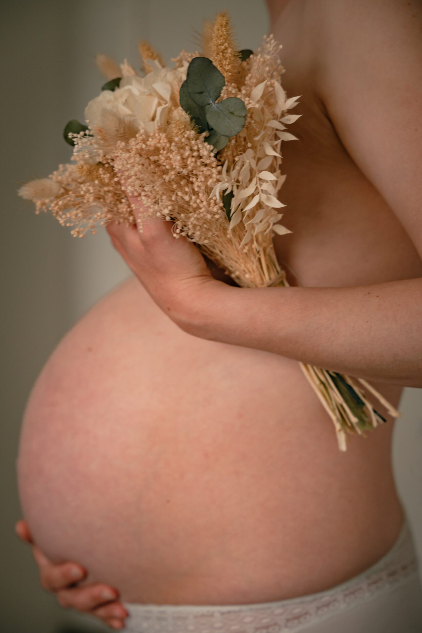 Focus sur le ventre d'une future mère enceinte qui tient un bouquet de fleurs