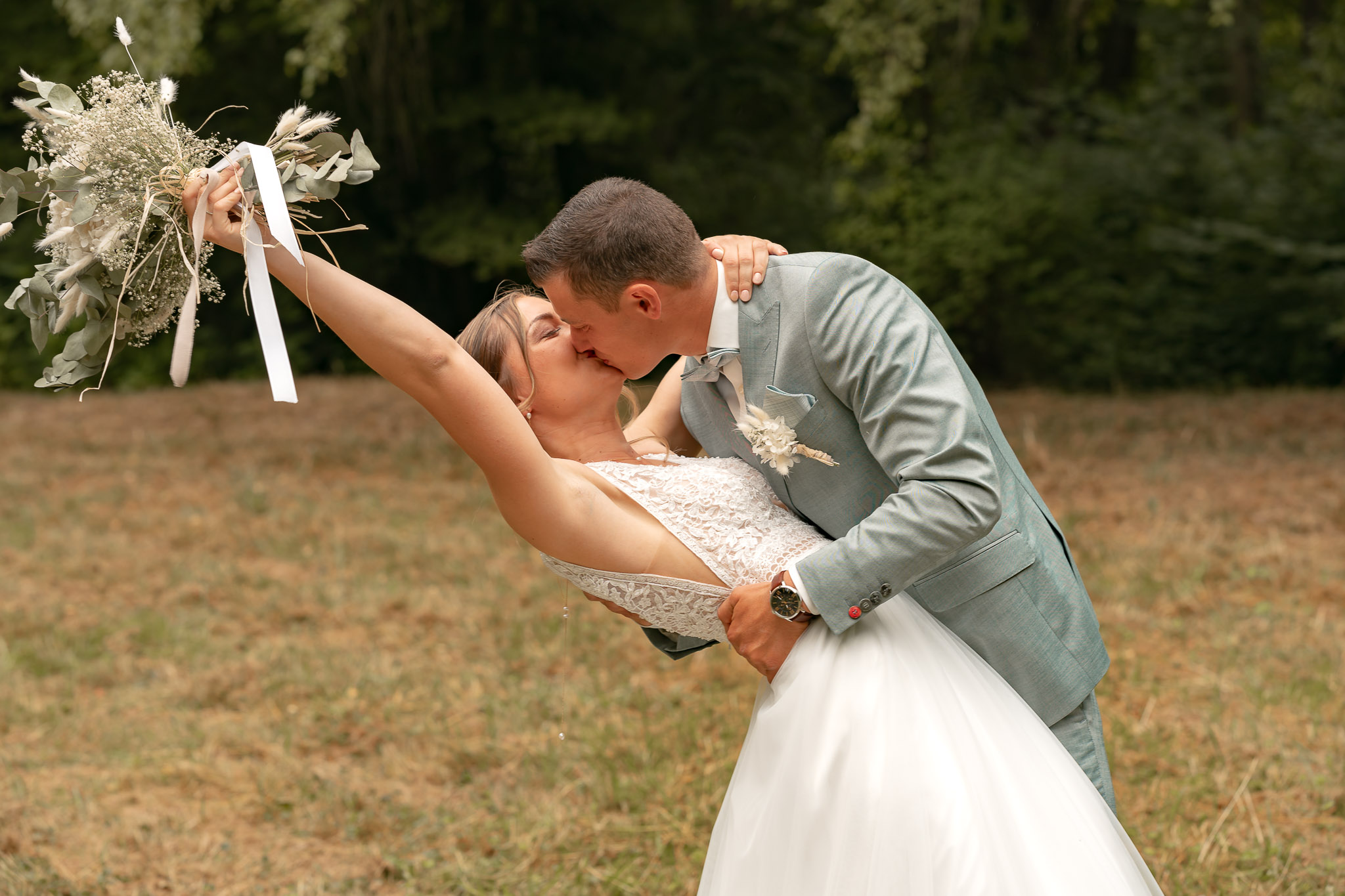Femme dans sa robe de mariée avec son mari qui la tient tendrement dans un parc