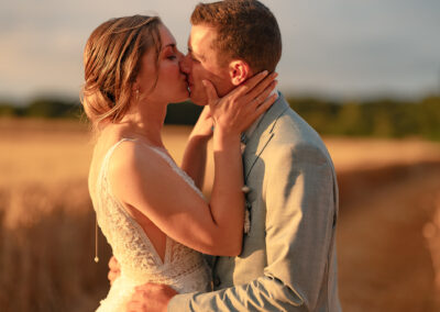 Photo romantique des mariés qui s'embrassent dans les champs au coucher du soleil